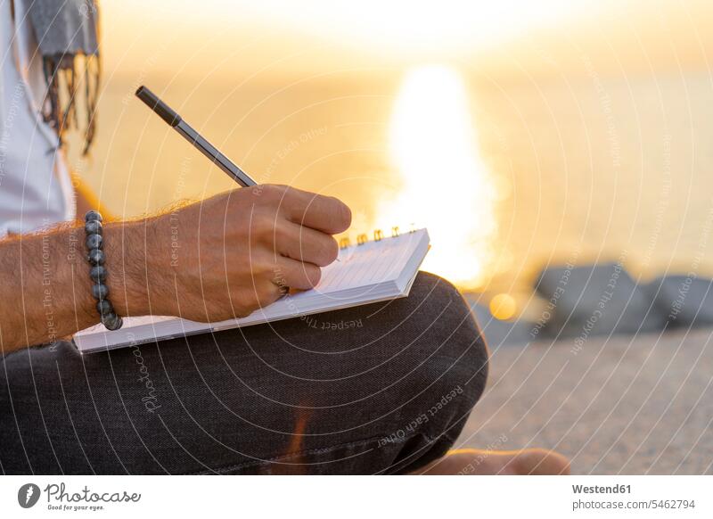 Spanien: Mann schreibt während des Sonnenaufgangs auf einem Notizbuch auf Felsen am Strand schreiben aufschreiben notieren schreibend Schrift Meer Meere