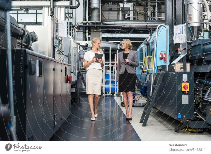 Zwei Frauen mit Tablette zu Fuß und im Gespräch in der Fabrik Fabrikhalle Industriehallen Fabrikhallen gehen gehend geht sprechen reden Fabriken weiblich