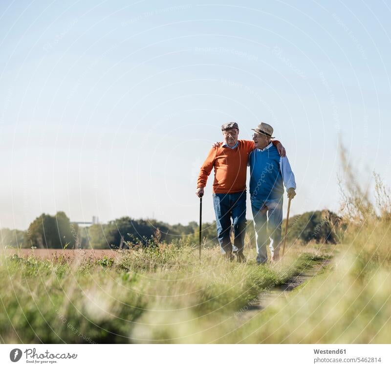 Zwei alte Freunde bei einem Spaziergang durch die Felder, die über alte Zeiten reden Arm umlegen Arme umlegen Beste Freunde Bester Freund gehen gehend geht