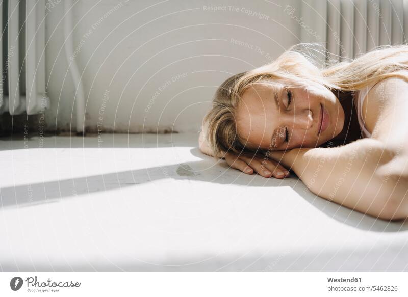 Bildnis einer blonden jungen Frau, die mit geschlossenen Augen auf dem Boden liegt Heizluefter Heizlüfter Radiator Radiatoren schlafend entspannen relaxen