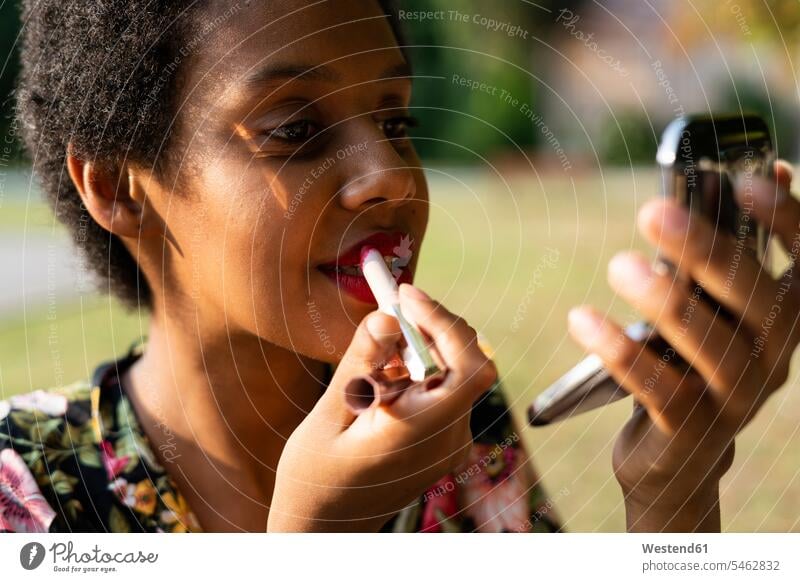 Porträt einer jungen Frau, die im Freien Lippenstift aufträgt Portrait Porträts Portraits anwenden auftragen Lippenstifte weiblich Frauen Beauty Schoenheit