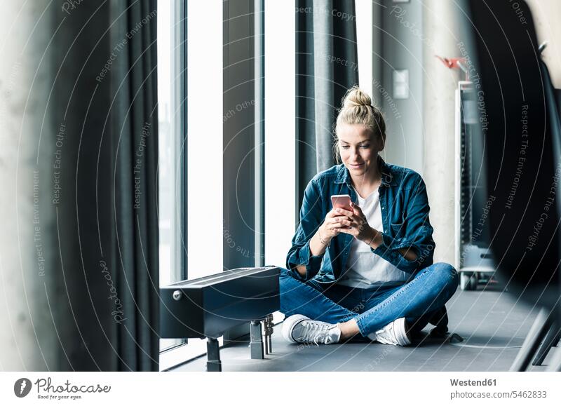 Geschäftsfrau sitzt auf dem Boden im Büro und benutzt ein Mobiltelefon Leute Menschen People Person Personen Europäisch Kaukasier kaukasisch 1 Ein ein Mensch