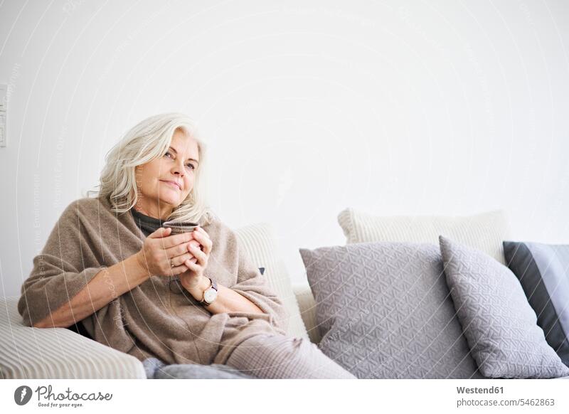 Nachdenklich Rentnerin hält Kaffeetasse, während auf dem Sofa gegen weiße Wand in der Wohnung sitzen Farbaufnahme Farbe Farbfoto Farbphoto Dänemark Skandinavien