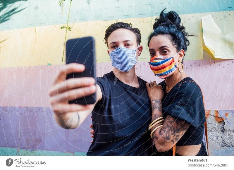 Lesbisches Paar, das in der Stadt mit Maske Selbsthilfe nimmt Farbaufnahme Farbe Farbfoto Farbphoto Außenaufnahme außen draußen im Freien Tag Tageslichtaufnahme