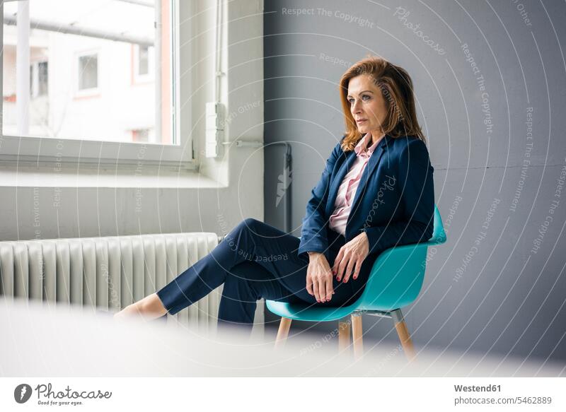 Unzufriedene Geschäftsfrau sitzt auf einem Stuhl neben dem Fenster in ihrem Büro ernst Ernst Ernsthaftigkeit ernsthaft verstimmt genervt ärgerlich aergerlich