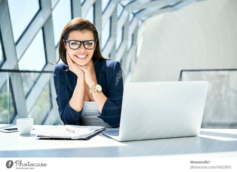 Porträt einer lächelnden Geschäftsfrau, die in einem modernen Büro am Schreibtisch sitzt Office Büros Arbeitstisch Schreibtische Geschäftsfrauen Businesswomen