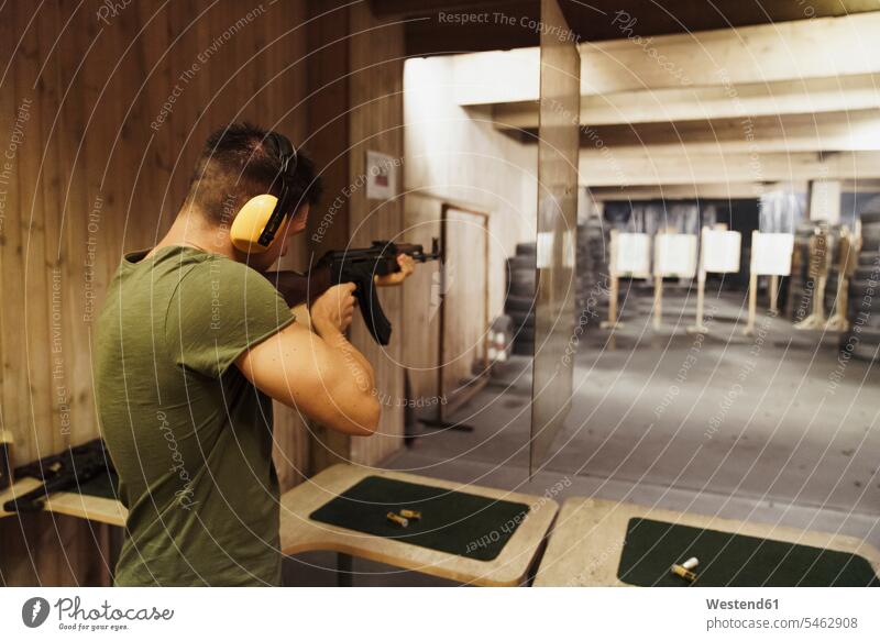 Mann zielt mit einem Gewehr in einer Indoor-Schießanlage Schusswaffe Gewehre Schießstand Schiessstaende Schießstände Schiessstand schießen zielen zielend Männer