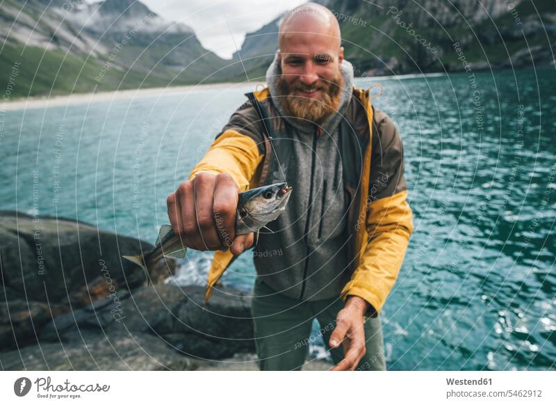 Norwegen, Lofoten, Moskenesoy, Junger Mann hält fangfrischen Fisch Angelhaken Fischhaken Fanghaken Haken Fische Pisces Horseid Beach Männer männlich Tier