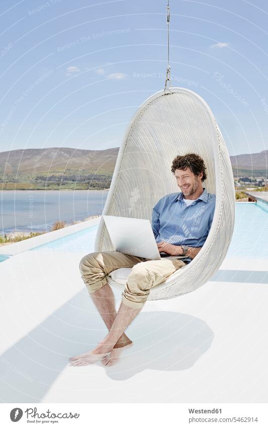 Mann sitzt in Hängesessel über dem Schwimmbad und benutzt Laptop Touristen geschäftlich Geschäftsleben Geschäftswelt Geschäftsperson Geschäftspersonen