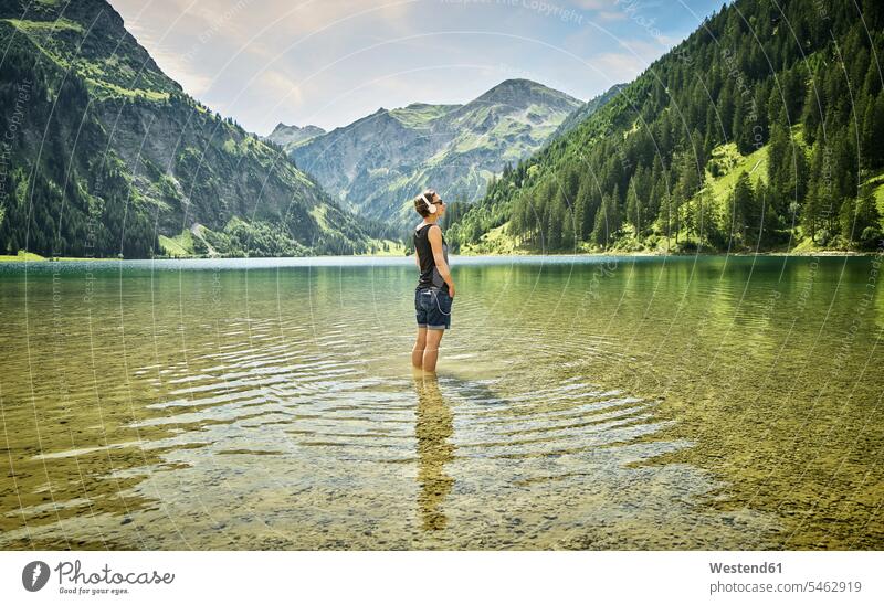 Reife Frau steht knietief im Vilsalpsee und hört an einem sonnigen Tag Musik Farbaufnahme Farbe Farbfoto Farbphoto Österreich Außenaufnahme außen draußen