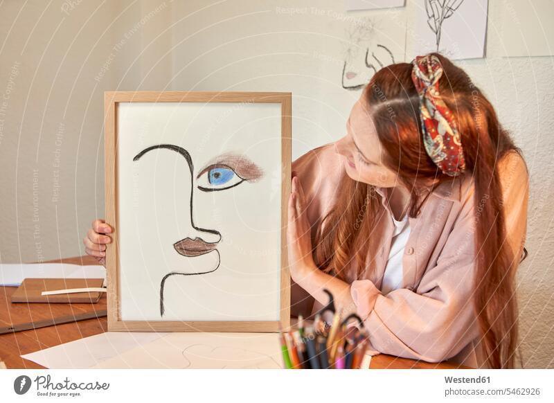 Weibliche Künstlerin zeigt Zeichnung Kunst Bilderrahmen gegen Wand zu Hause Farbaufnahme Farbe Farbfoto Farbphoto Innenaufnahme Innenaufnahmen innen drinnen