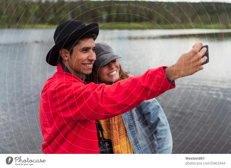 Finnland, Lappland, glückliches Paar macht ein Selfie an einem See Seen Pärchen Paare Partnerschaft Glück glücklich sein glücklichsein Selfies Gewässer Wasser