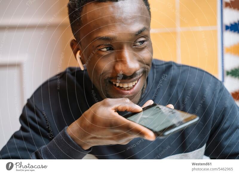 Porträt eines lächelnden jungen Mannes mit drahtlosen Kopfhörern am Telefon Handy Mobiltelefon Handies Handys Mobiltelefone Erreichbarkeit verfügbar
