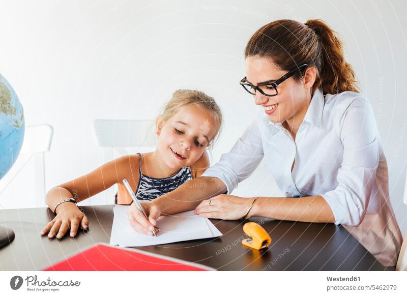 Lehrer hilft Schulmädchen am Schreibtisch schreiben auf Papier Europäer zwei Personen Mädchen 8-9 Jahre junge Frau 25-30 Jahre Europäerin Lehrerin lächeln