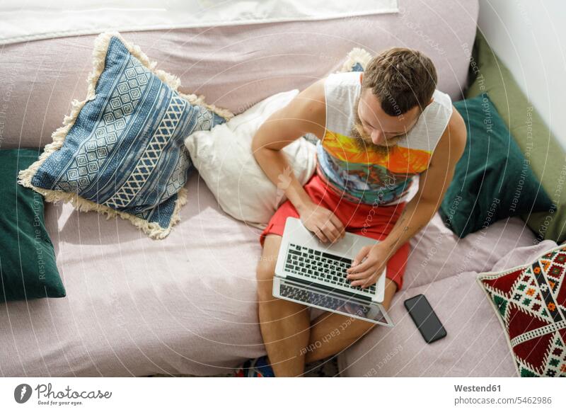 Mann benutzt Laptop auf Sofa im Wohnzimmer zu Hause Farbaufnahme Farbe Farbfoto Farbphoto Innenaufnahme Innenaufnahmen innen drinnen Tag Tageslichtaufnahme
