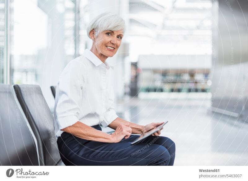 Lächelnde ältere Geschäftsfrau sitzt im Wartebereich und benutzt ein Tablet Geschäftsfrauen Businesswomen Businessfrauen Businesswoman Tablet Computer Tablet-PC