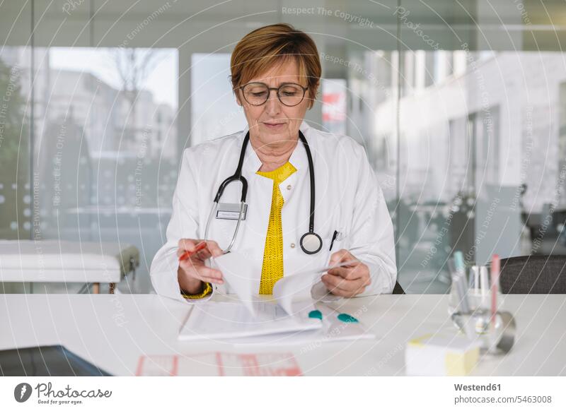 Arzt sitzt am Schreibtisch und prüft Dokumente Job Berufe Berufstätigkeit Beschäftigung Jobs Papiere Unterlagen Glasscheiben Gesundheit Gesundheitswesen