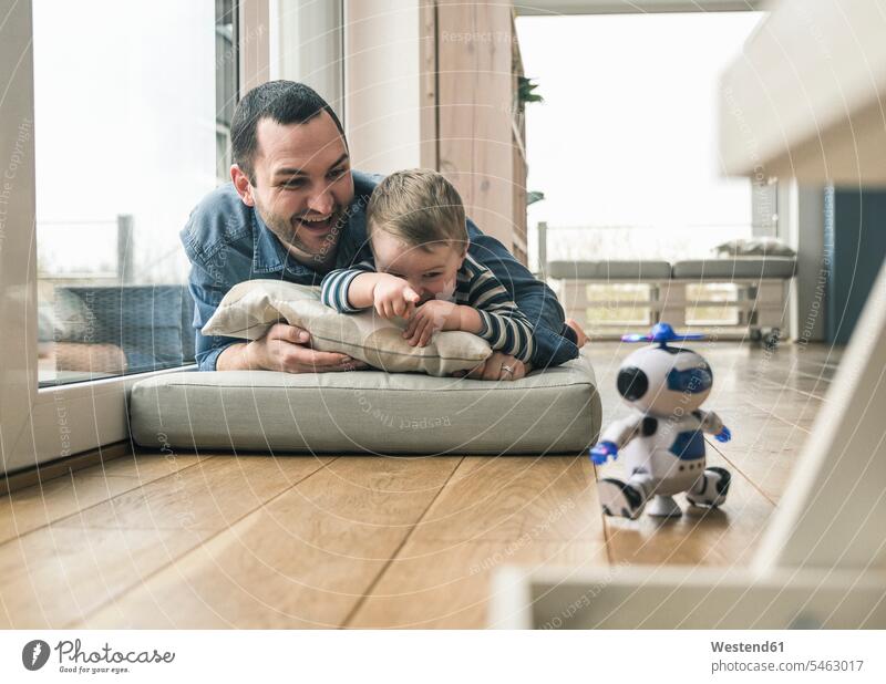 Aufgeregter Vater und Sohn liegen auf einer Matratze zu Hause und beobachten einen Spielzeugroboter Zuhause daheim liegend liegt Aufregung aufregend