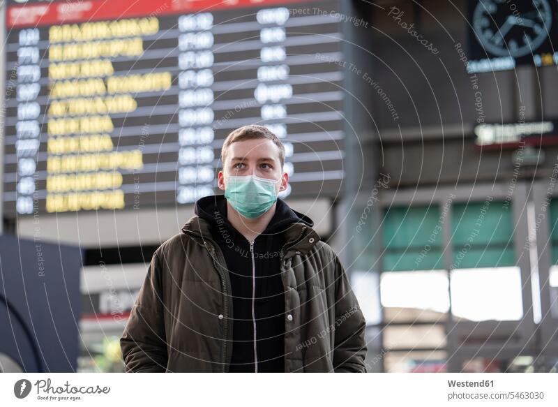 Junger Mann mit Gesichtsmaske am Bahnhof in der Stadt Anzeigetafeln Display Gesundheit Gesundheitswesen medizinisch geschützt schützen Absicherung außen draußen