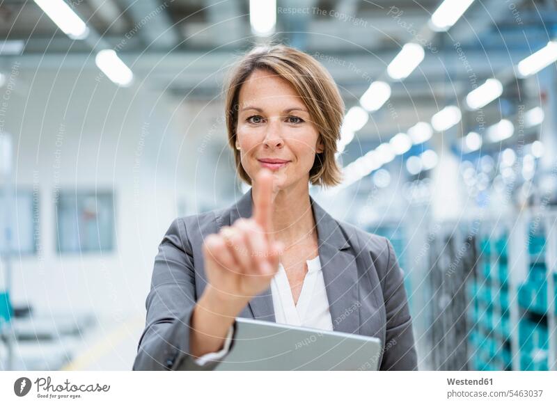Porträt einer Geschäftsfrau mit Tablet in einer modernen Fabrik, die einen virtuellen Bildschirm berührt Leute Menschen People Person Personen Europäisch
