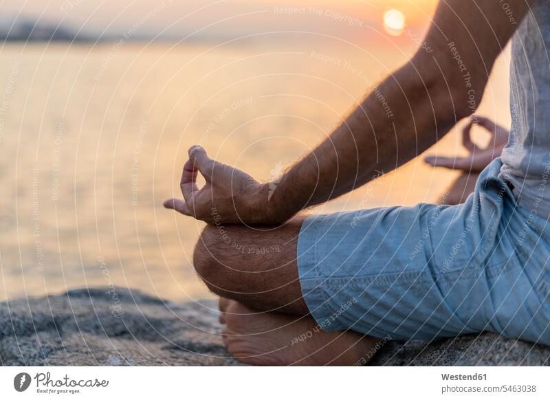 Spanien: Mann meditiert während des Sonnenaufgangs an felsigem Strand, Mudra sitzen sitzend sitzt Männer männlich Meditation meditieren Handhaltung Handstellung