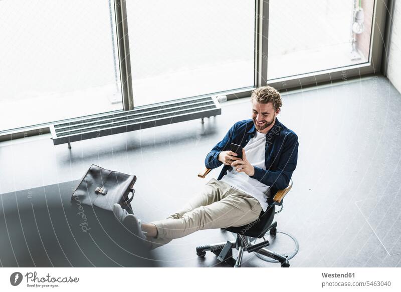 Lächelnd lässig Geschäftsmann sitzt im Büro mit Füßen oben mit Handy Businessmann Businessmänner Geschäftsmänner Office Büros sitzen sitzend Mobiltelefon