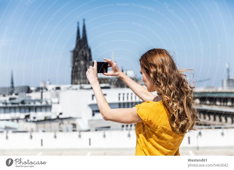 Deutschland, Köln, Frau beim Fotografieren mit Smartphone auf der Dachterrasse weiblich Frauen iPhone Smartphones fotografieren Dachterrassen Erwachsener