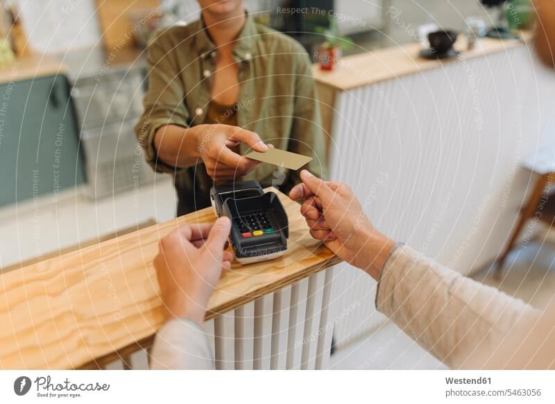Mittelsektion einer Unternehmerin, die dem Kunden an der Kasse im Café eine Kreditkarte gibt Farbaufnahme Farbe Farbfoto Farbphoto Innenaufnahme Innenaufnahmen