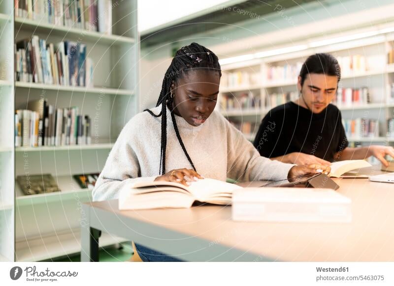 Zwei Studenten lernen in einer Bibliothek Freunde Buch Tisch lesen sitzen studieren Gemeinsam Konzentration Lifestyle Innenaufnahme klug clever Technologie