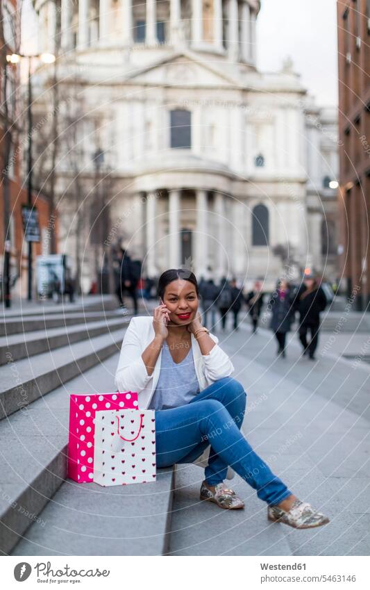 Großbritannien, London, Frau mit Einkaufstaschen am Handy auf einer Treppe in der Stadt sitzend Shopping einkaufen shoppen sitzt telefonieren anrufen Anruf