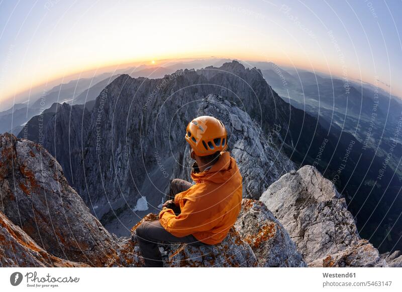 Kletterer mit orangefarbenem Helm auf der Ellmauer Halt bei Sonnenaufgang sitzend, Wilder Kaiser, Ellmauer Halt, Tirol, Österreich sitzt früh Frühe Morgen