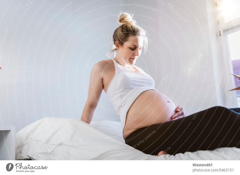 Schwangere Frau sitzt zu Hause auf dem Bett Betten anfassen Berührung sitzend entspannen relaxen entspanntheit relaxt daheim schwangere Frau Muße Raum Räume