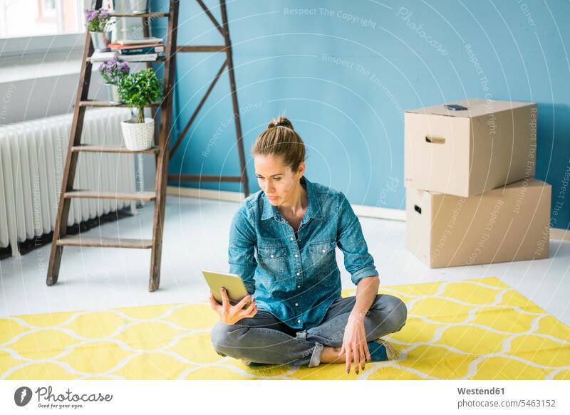Frau sitzt auf dem Boden ihrer neuen Wohnung und benutzt ein digitales Tablett Tablet Computer Tablet-PC Tablet PC iPad Tablet-Computer sitzen sitzend Umbau