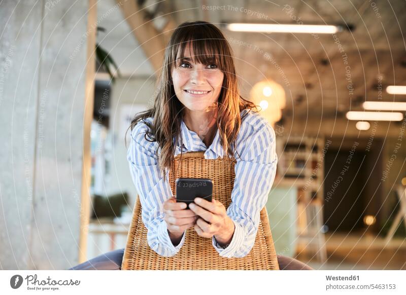Reife Frau lächelt, während sie zu Hause ein Smartphone benutzt Farbaufnahme Farbe Farbfoto Farbphoto Innenaufnahme Innenaufnahmen innen drinnen Tag