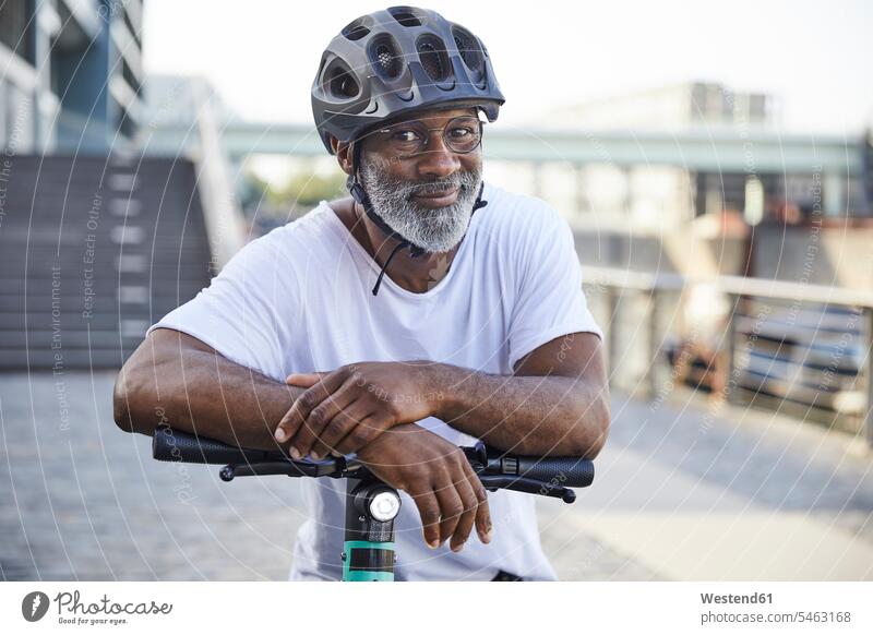 Porträt eines lächelnden reifen Mannes mit Fahrradhelm, der sich auf den Lenker eines Elektrorollers stützt Leute Menschen People Person Personen gemischtrassig
