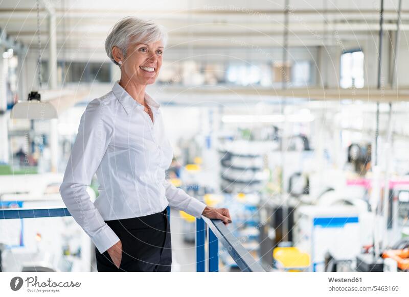 Lächelnde ältere Geschäftsfrau im Obergeschoss einer Fabrik mit Blick auf den Verkaufsraum Fabriken Geschäftsfrauen Businesswomen Businessfrauen Businesswoman
