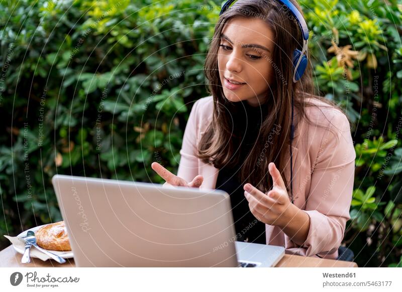 Geschäftsfrau gestikuliert bei Videogesprächen über Laptop auf der Terrasse eines Cafés Farbaufnahme Farbe Farbfoto Farbphoto Tag Tageslichtaufnahme
