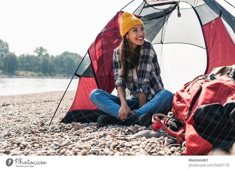 Glückliche junge Frau sitzt in einem Zelt am Flussufer glücklich glücklich sein glücklichsein Zelte sitzen sitzend lächeln weiblich Frauen Ufer Erwachsener