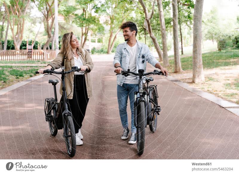 Lächelndes junges Paar mit Elektrofahrrädern auf der Straße Farbaufnahme Farbe Farbfoto Farbphoto Spanien E-Bike Elektrorad eBike Elektrofahrrad eBikes E-Bikes
