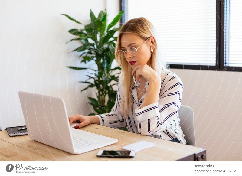 Blonde Büroangestellte, die am Schreibtisch sitzt und einen Laptop benutzt sitzen sitzend Arbeitstisch Schreibtische blond blonde Haare blondes Haar