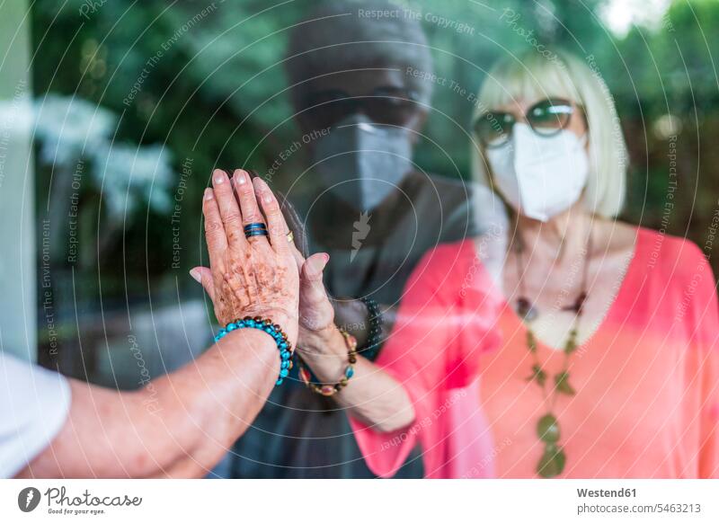 Hand einer älteren Frau berührt eine Freundin durch ein Fenster während der Ausgangssperre Farbaufnahme Farbe Farbfoto Farbphoto Spanien Freizeitkleidung
