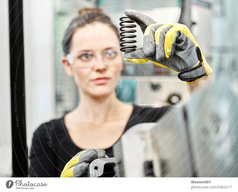 Frau arbeitet an einer Maschine, schaut auf die Feder herstellen produzieren Herstellung braune Haare braunhaarig brünett braunes Haar Metall Metalle
