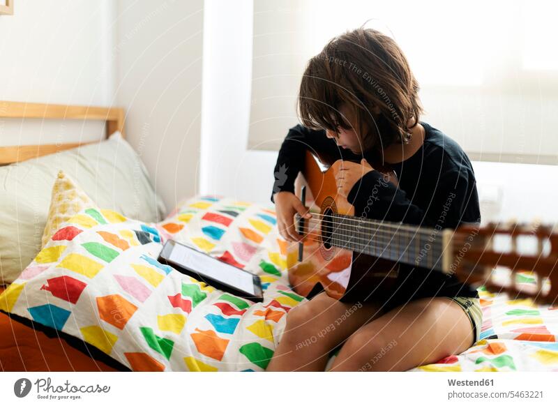 Junge sitzt auf dem Bett und benutzt digitales Tablett zum Spielen von Liedern auf der Gitarre Instrument Instrumente Musikinstrumente Saiteninstrumente