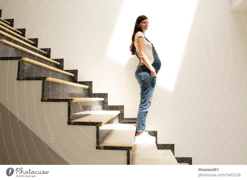 Nachdenkliche schwangere Frau schaut weg, während sie auf einer Treppe im neuen Haus steht Farbaufnahme Farbe Farbfoto Farbphoto Deutschland Innenaufnahme