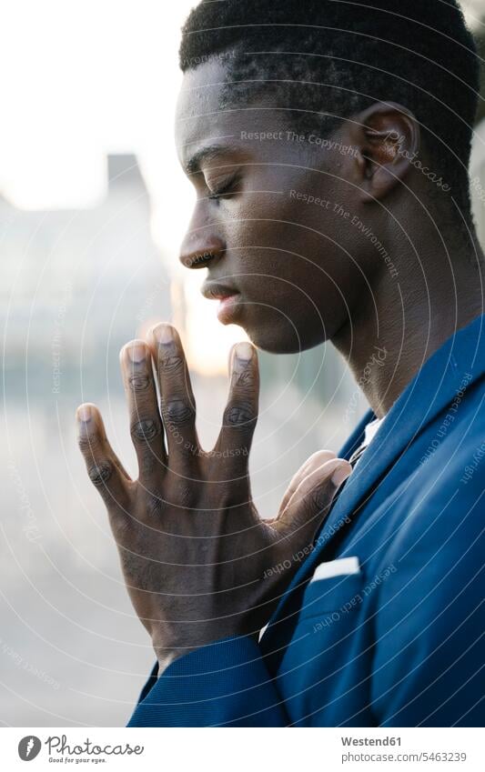 Junger Mann mit verschränkten Händen und geschlossenen Augen im Freien stehend Farbaufnahme Farbe Farbfoto Farbphoto Außenaufnahme außen draußen Tag