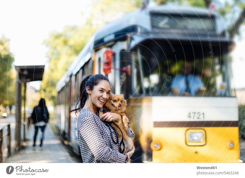 Glückliche junge Frau mit Hund an der Straßenbahnhaltestelle in der Stadt Tiere Tierwelt Haustiere Hunde Transport Transportwesen Bahnen Straßenbahnen Tram