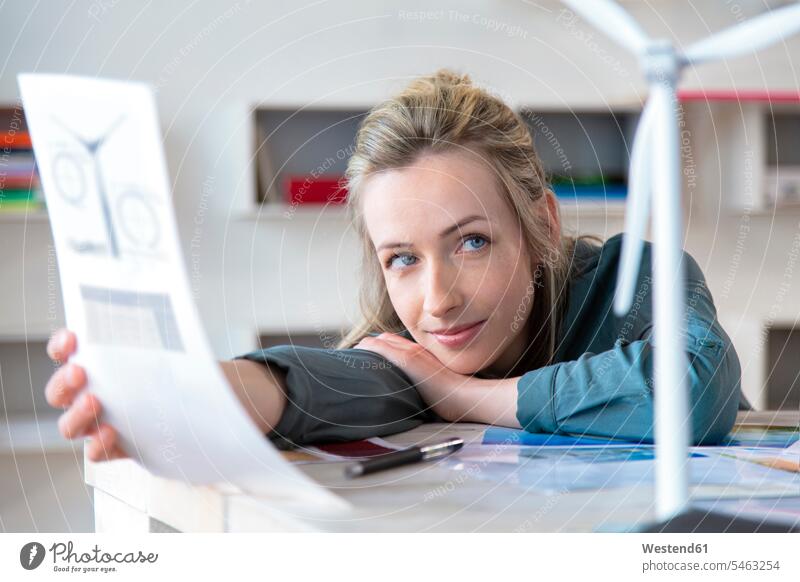 Porträt einer am Schreibtisch lehnenden Frau im Büro mit Papier und Modell einer Windkraftanlage Leute Menschen People Person Personen Europäisch Kaukasier