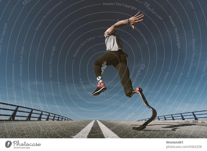 Behinderter Sportler mit Beinprothese beim Training auf der Strasse rennen springen Spruenge Sprünge hüpfen ausüben trainieren Übung geschwind Schnelligkeit fit