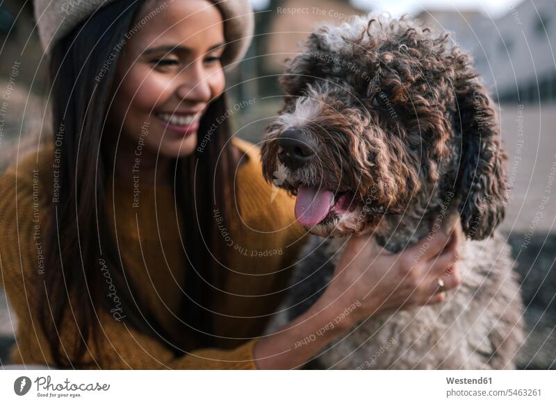 Glückliche junge Frau streichelt ihren Hund in der Stadt Freunde Kameradschaft Tiere Tierwelt Haustiere Hunde Mützen freuen Frohsinn Fröhlichkeit Heiterkeit
