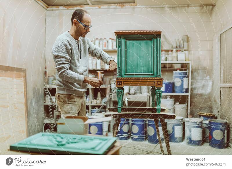 Handwerker repariert Möbel, während er in der Werkstatt steht Farbaufnahme Farbe Farbfoto Farbphoto Innenaufnahme Innenaufnahmen innen drinnen restaurieren